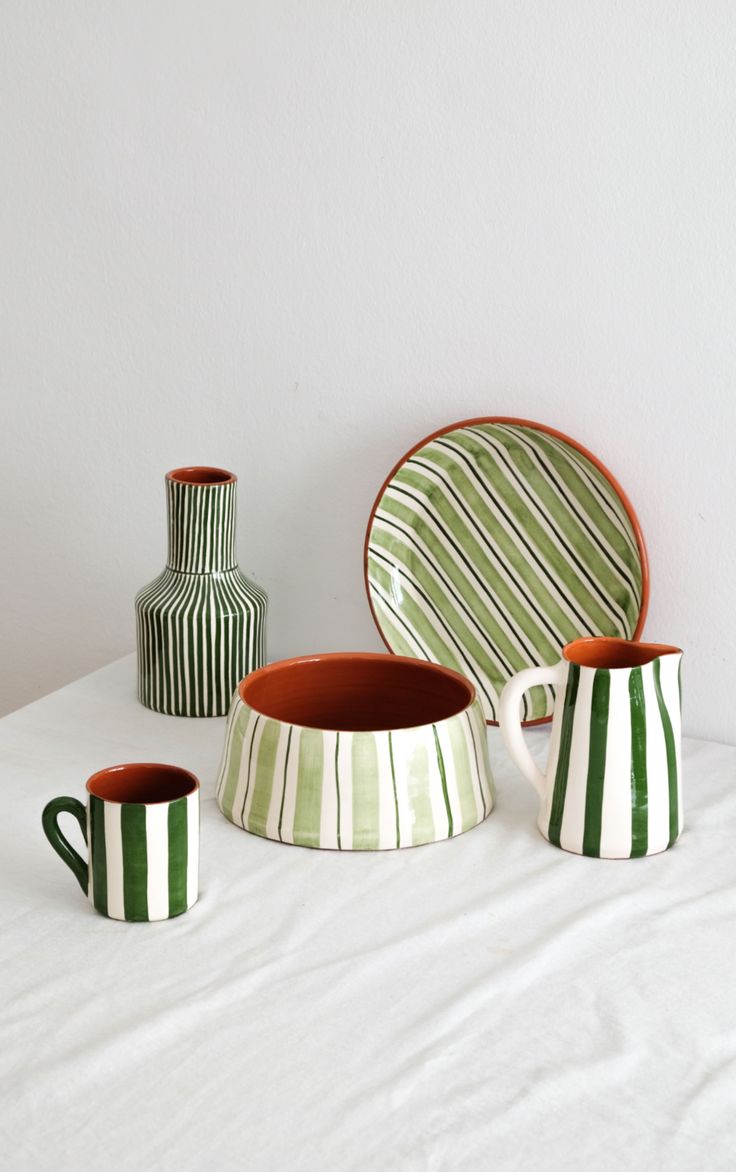 three green and white striped vases sitting on top of a table next to plates