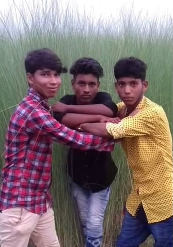 three young men are standing in front of tall grass and one is holding his arm around the other