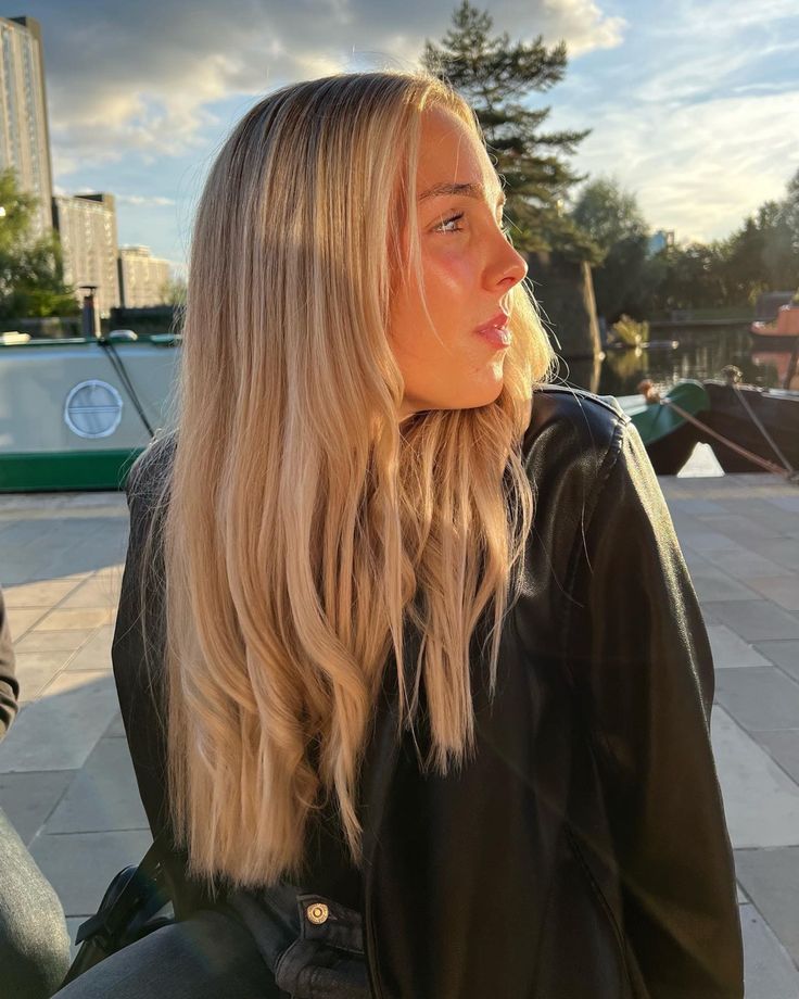 a woman with long blonde hair is sitting on a bench and looking off into the distance