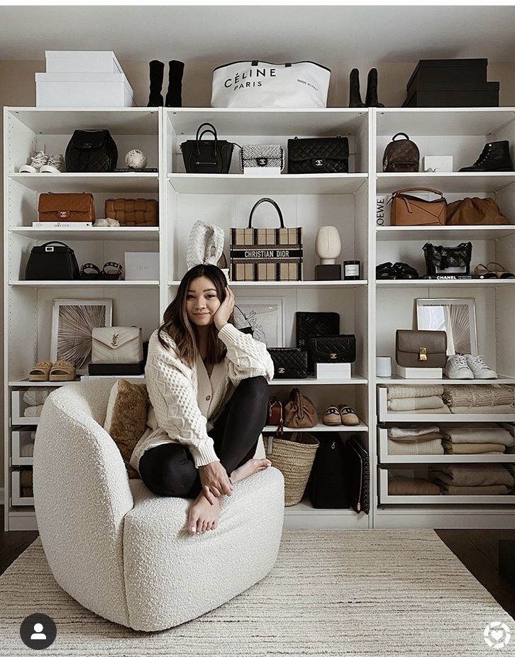 a woman sitting on a chair in front of a white book shelf filled with purses