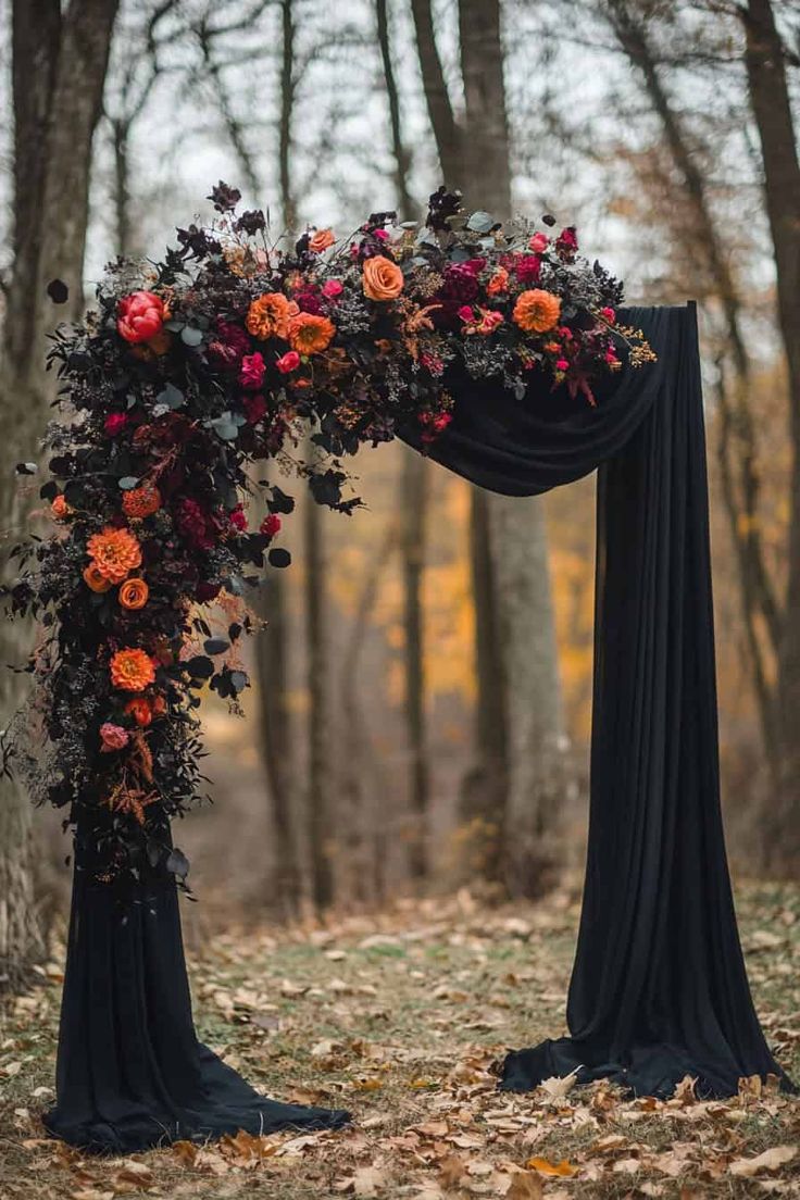 an arch decorated with flowers and greenery in the middle of a forest during fall