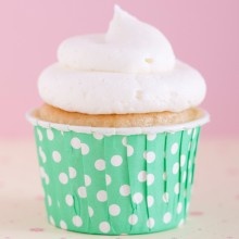 a cupcake with white frosting and sprinkles is on a green polka dot paper wrapper