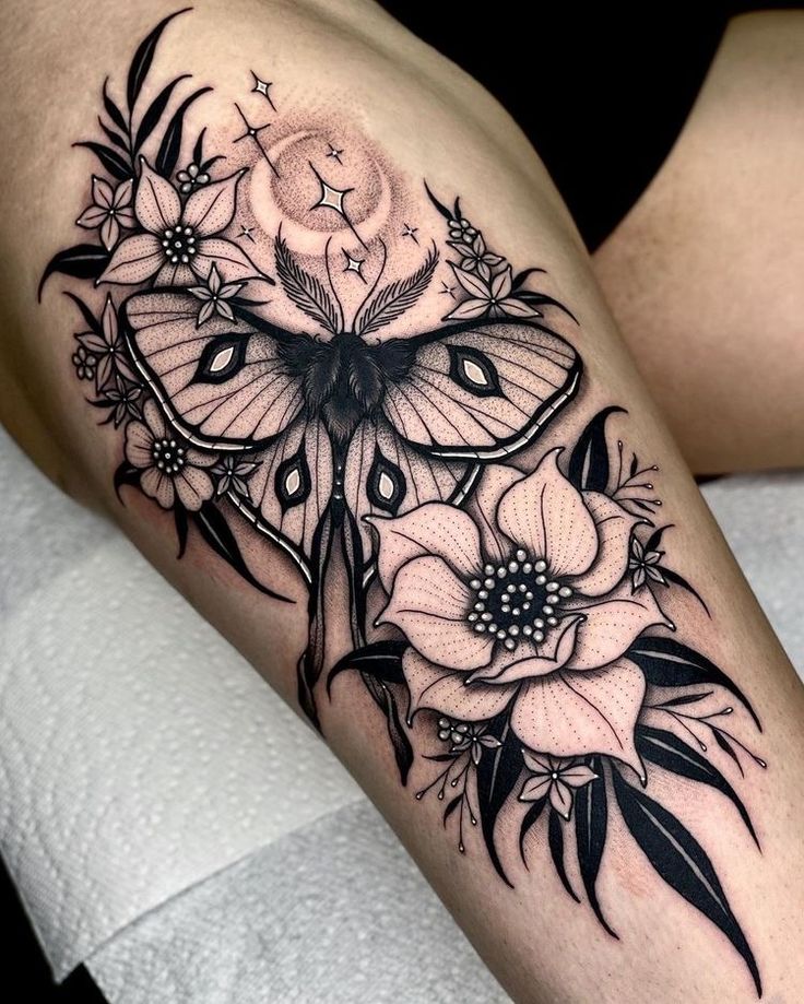 a woman's thigh with a butterfly and flowers tattoo on her leg, which is black and white