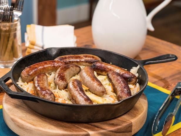 sausages are cooked in a skillet on a wooden board with utensils