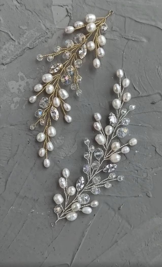 two pieces of jewelry sitting on top of a gray surface, one with pearls and the other with leaves