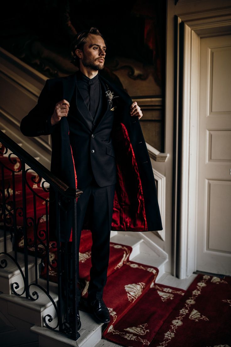 a man in a black suit and red tie standing at the top of some stairs