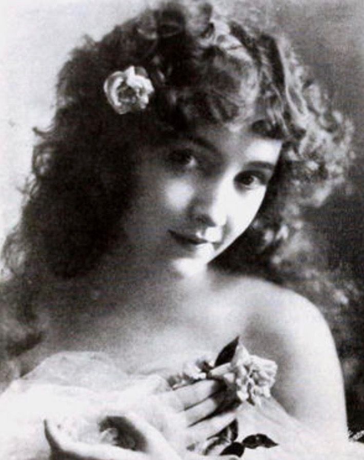 an old black and white photo of a woman with flowers in her hair holding a flower