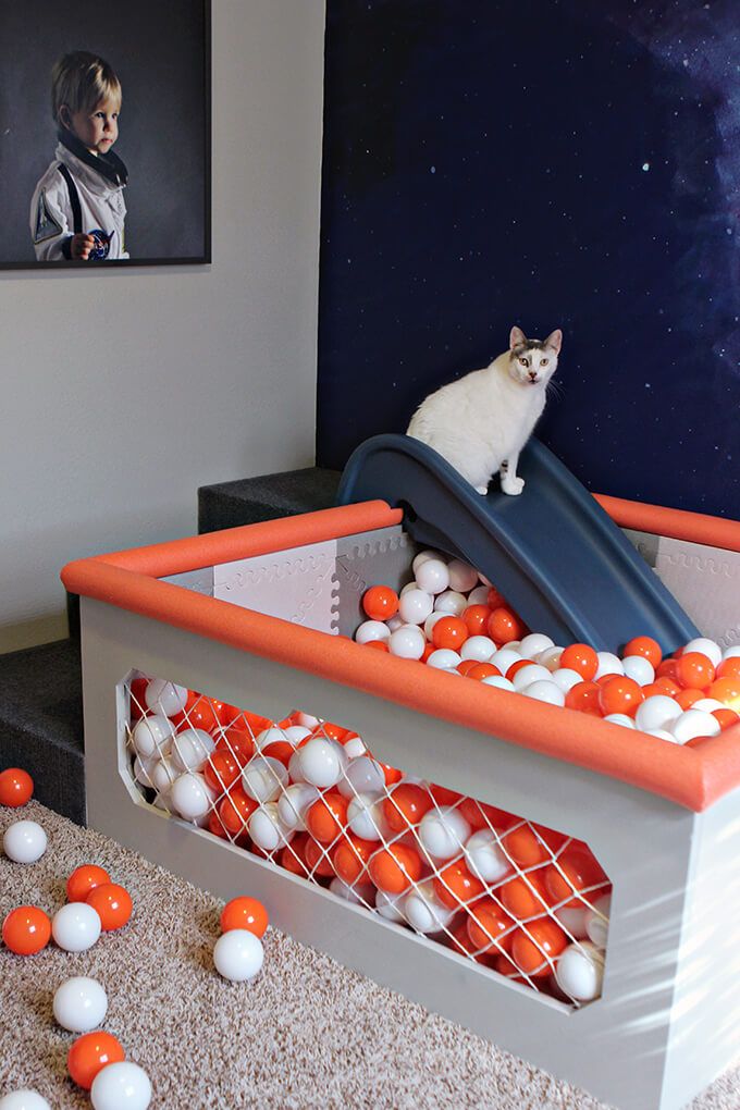 a white cat sitting on top of a slide in a room filled with orange and white balls