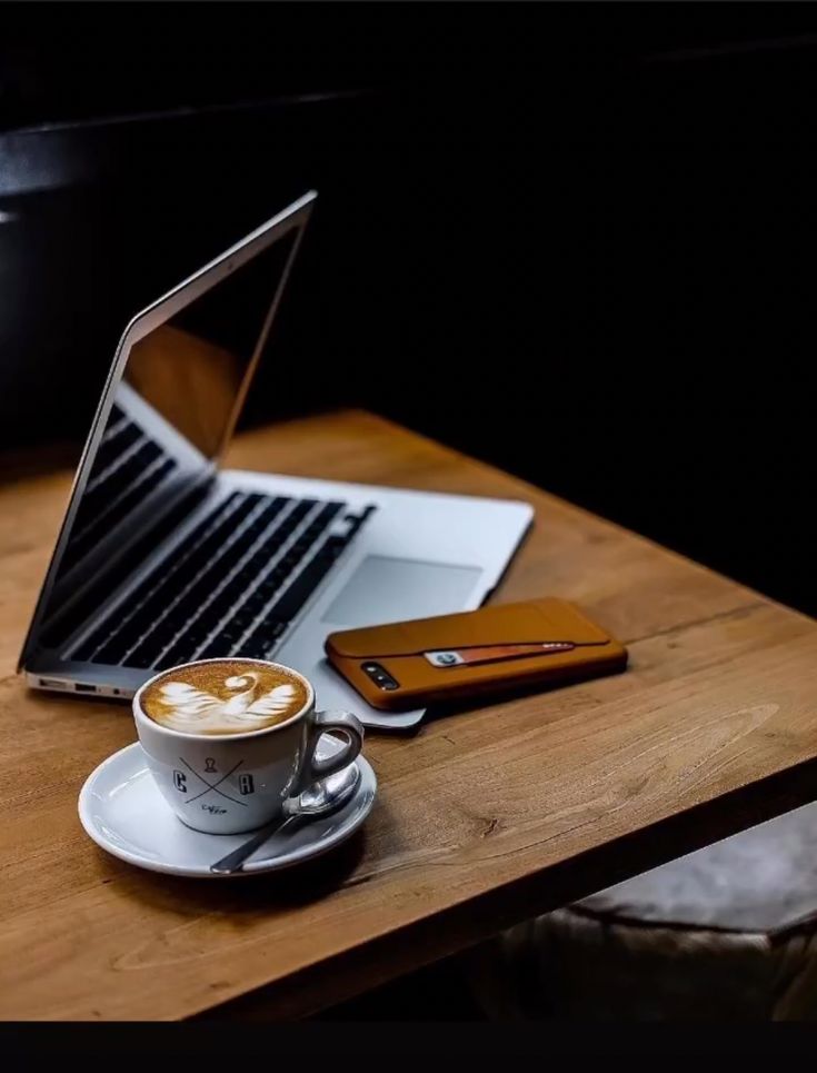 a laptop computer sitting on top of a wooden table next to a cup of coffee