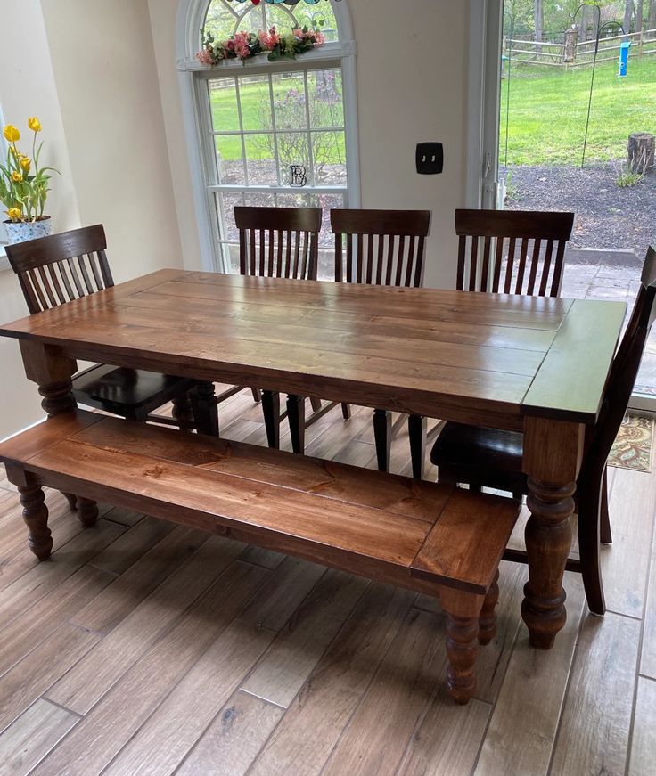 a dining room table and bench in front of a large window with flowers on it