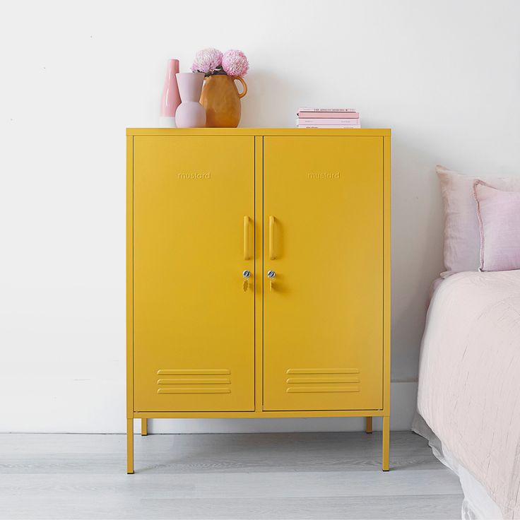 a yellow locker next to a bed with pink pillows and flowers on the top shelf