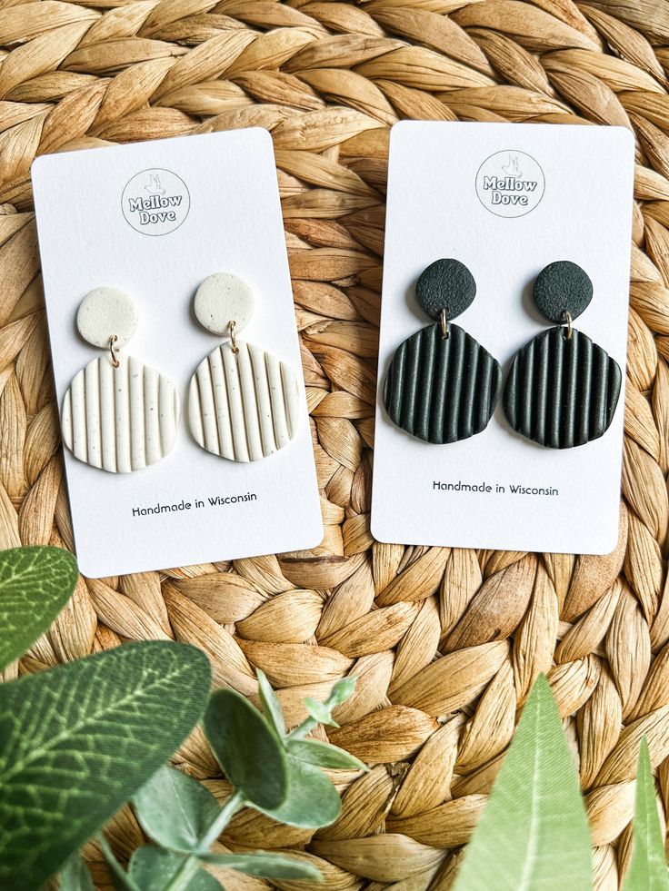 two pairs of earrings sitting on top of a woven basket next to a potted plant