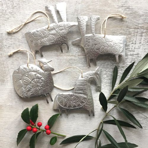 four ornaments are sitting on a table next to some leaves and holly branches with red berries