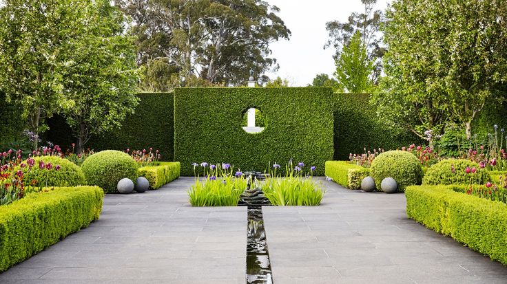 an outdoor garden with hedges and water feature