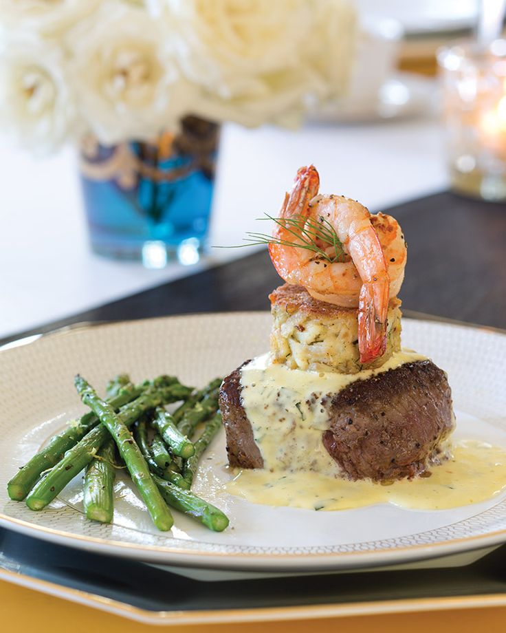 a white plate topped with meat and shrimp next to asparagus on a table