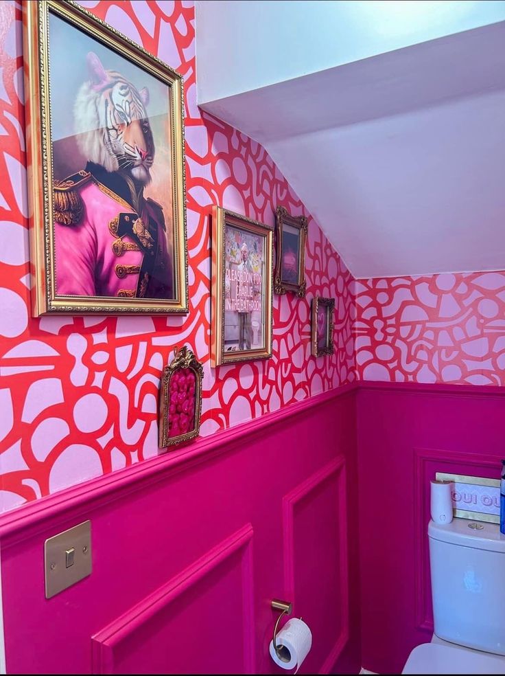 a bathroom decorated in pink and orange with pictures on the wall above the toilet area