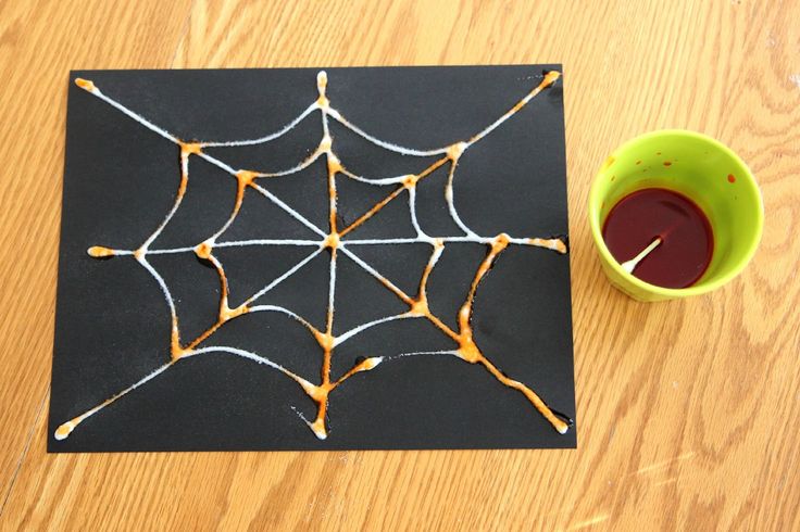 a spider web on a piece of black paper next to a cup of red liquid