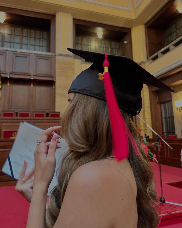 a woman wearing a graduation cap and gown writing on a piece of paper in her hand