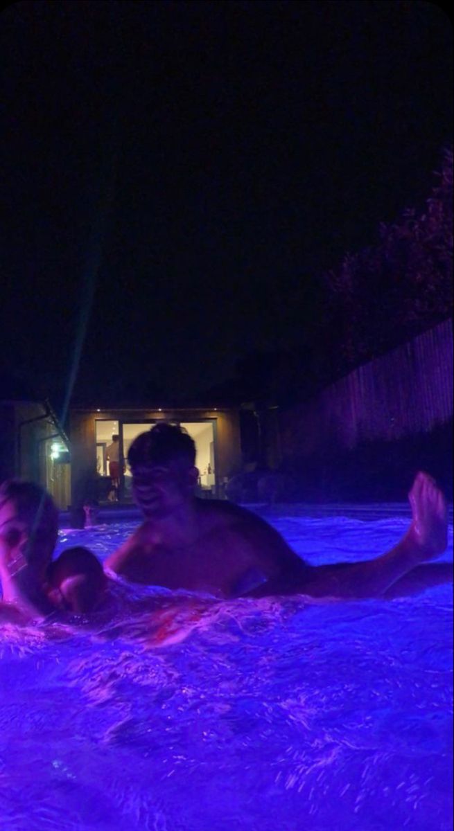 two people in the water at night with purple lights on them and one person holding his arm out