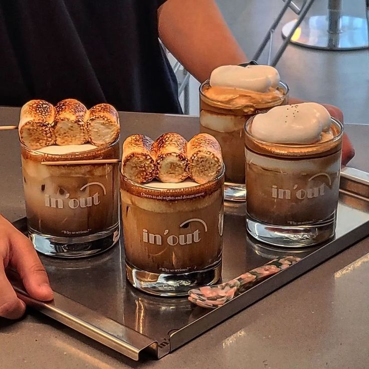 three glasses filled with different kinds of desserts on top of a metal tray in front of a person