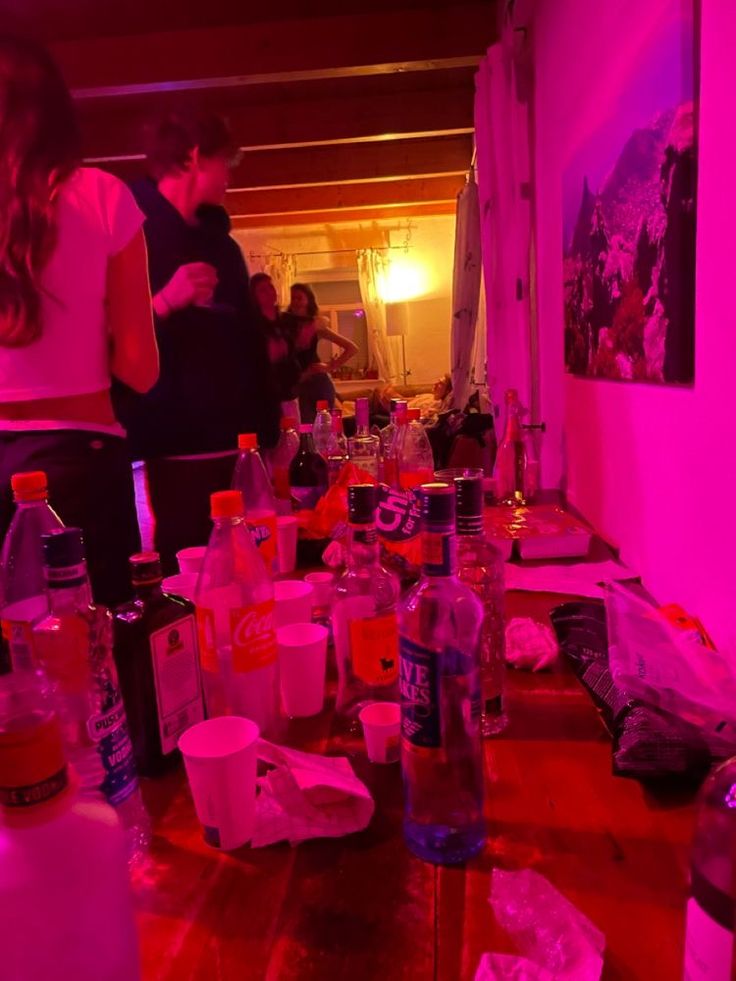 a group of people standing around a table with bottles and cups on top of it