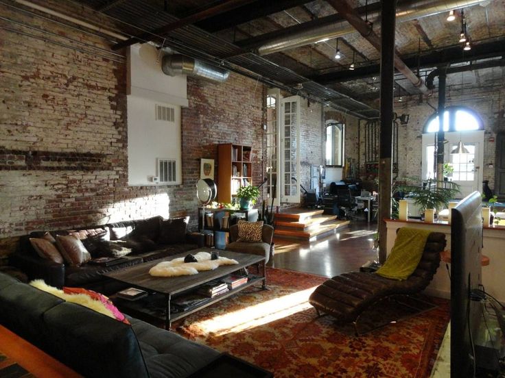 a living room filled with furniture and lots of windows next to a brick wall in an industrial building