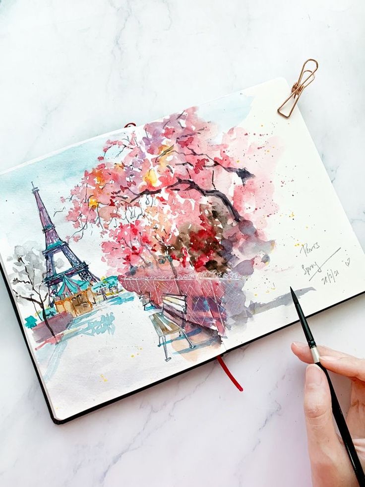 a person is holding a pencil and drawing in front of the eiffel tower