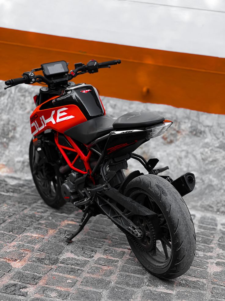 a red and black motorcycle parked on top of a brick road next to a fence