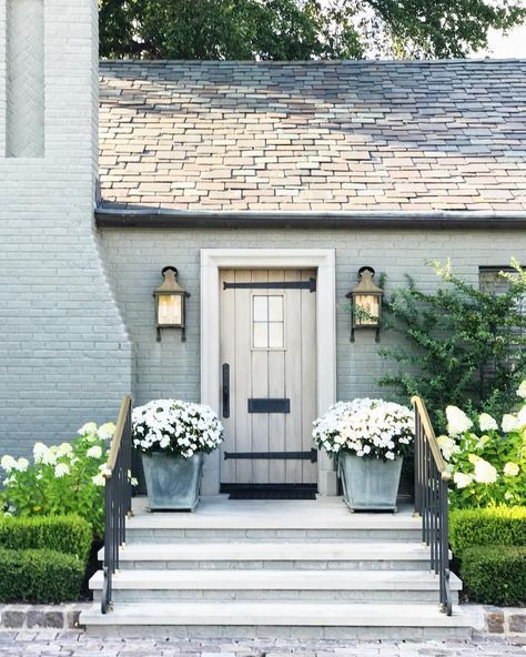 two planters with white flowers are on the front steps of a gray brick house