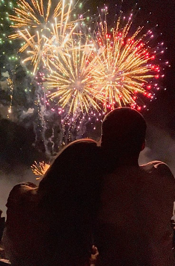 two people are looking at fireworks in the sky with their backs turned to the camera