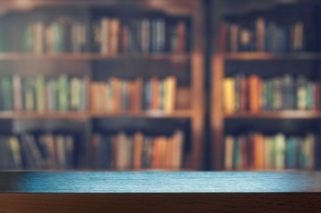 blurry image of bookshelves in library with wooden table top and blurred background