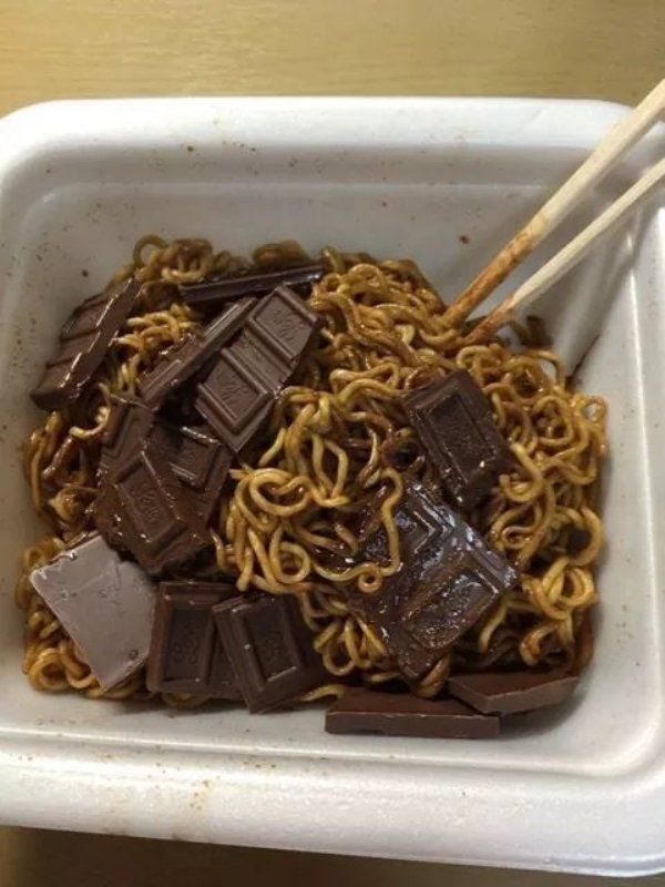 some noodles and chopsticks in a white container with brown stuff on top,