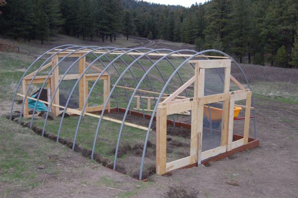 a small wooden greenhouse in the middle of a field