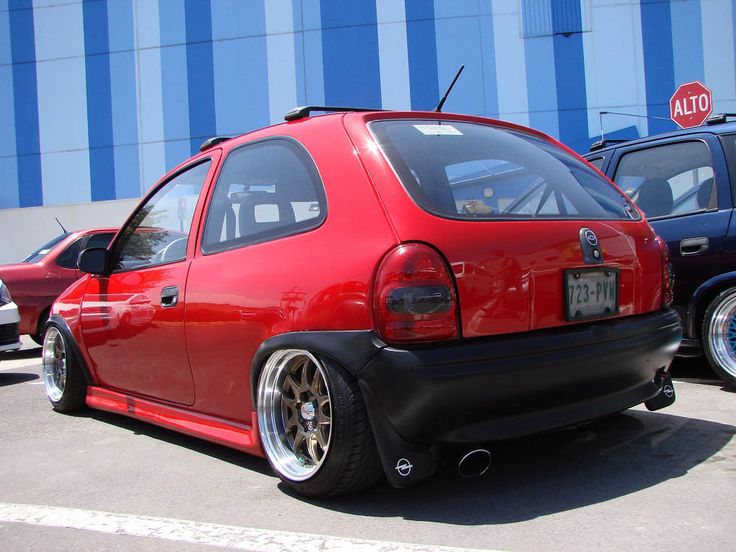 a red car parked next to other cars in a parking lot near a blue building