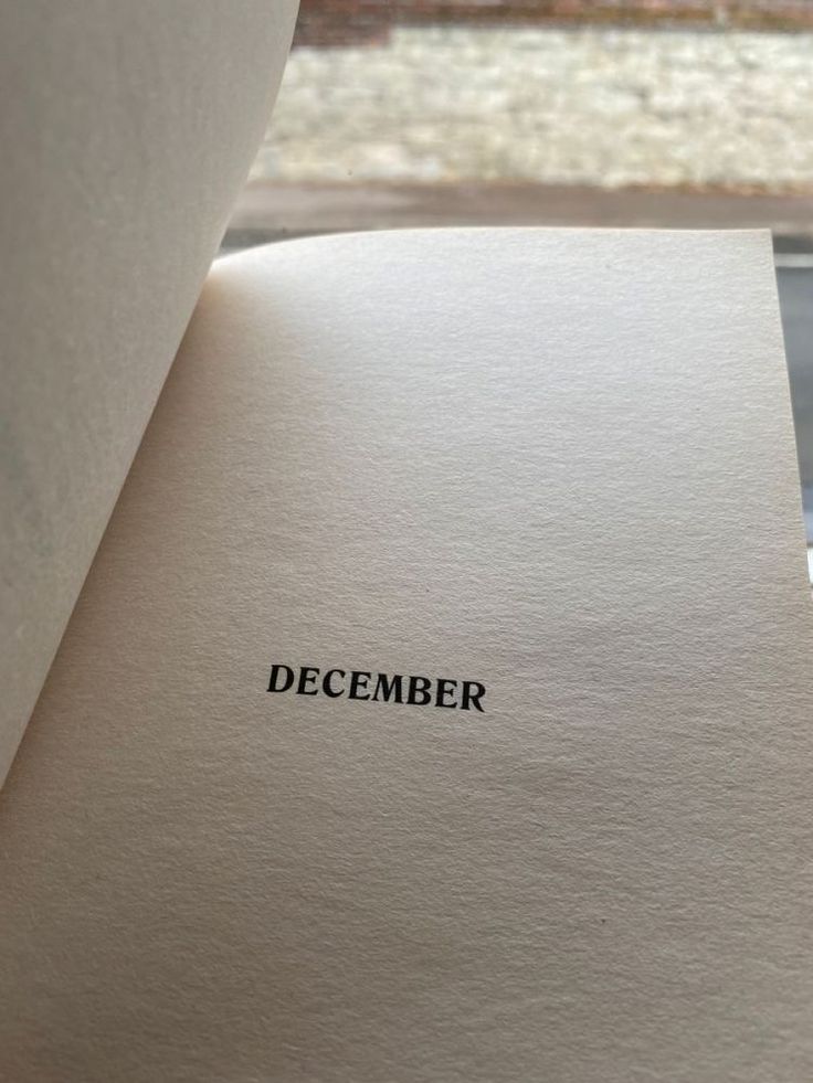 an open book with the word december printed on it, sitting next to a window