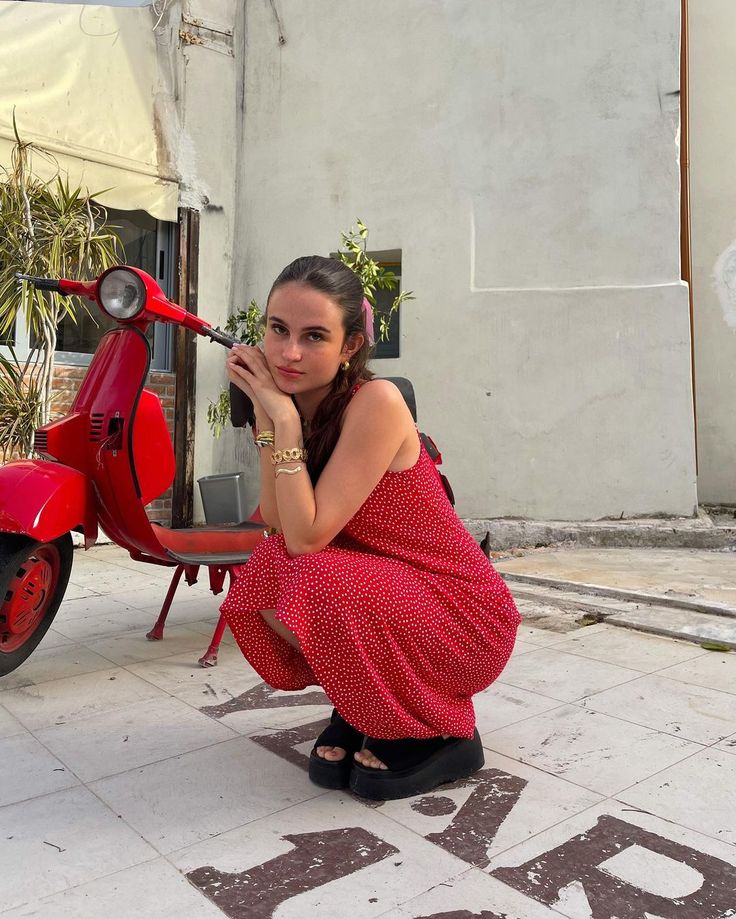 a woman kneeling down next to a red scooter