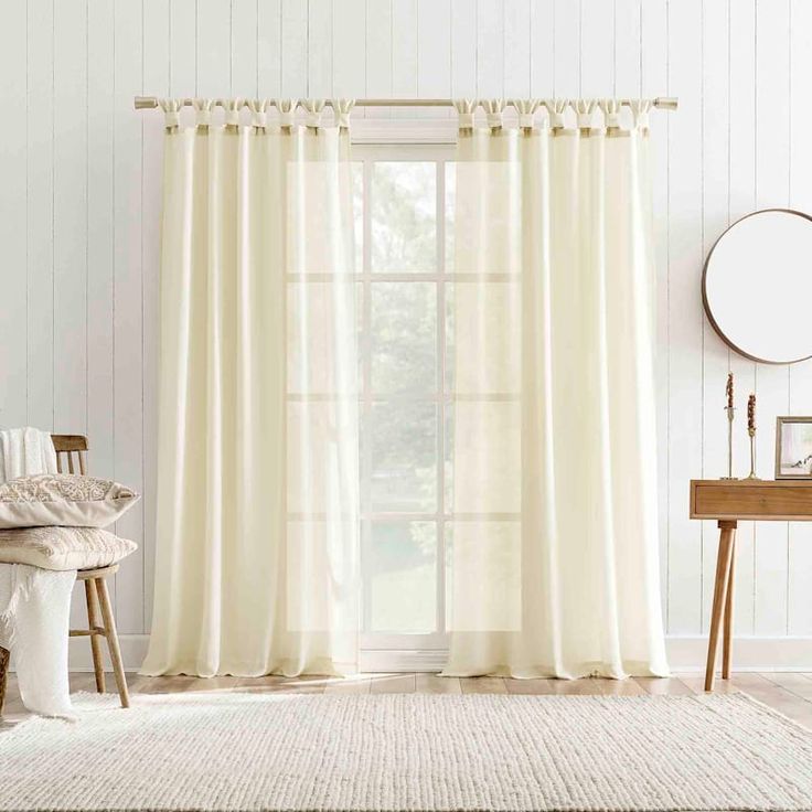 a living room with white walls and curtains on the window sill, a chair, mirror