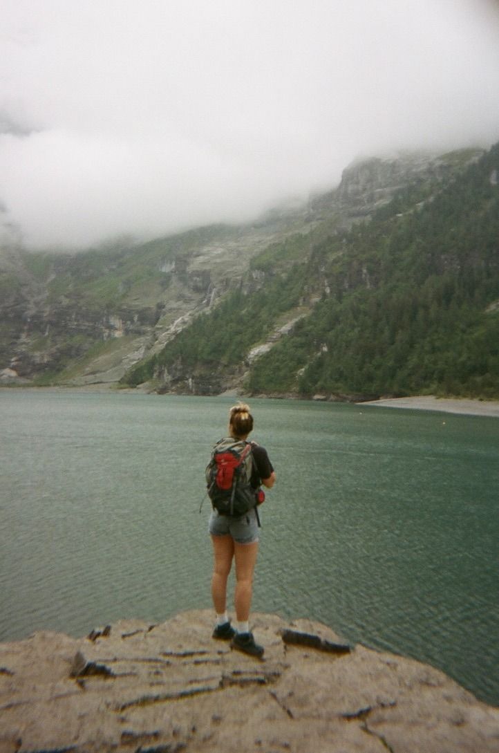 a woman standing on top of a cliff next to a body of water with mountains in the background