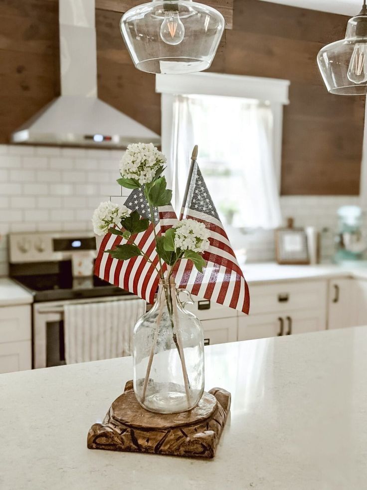 an american flag in a glass vase on a kitchen counter with hanging lights above it