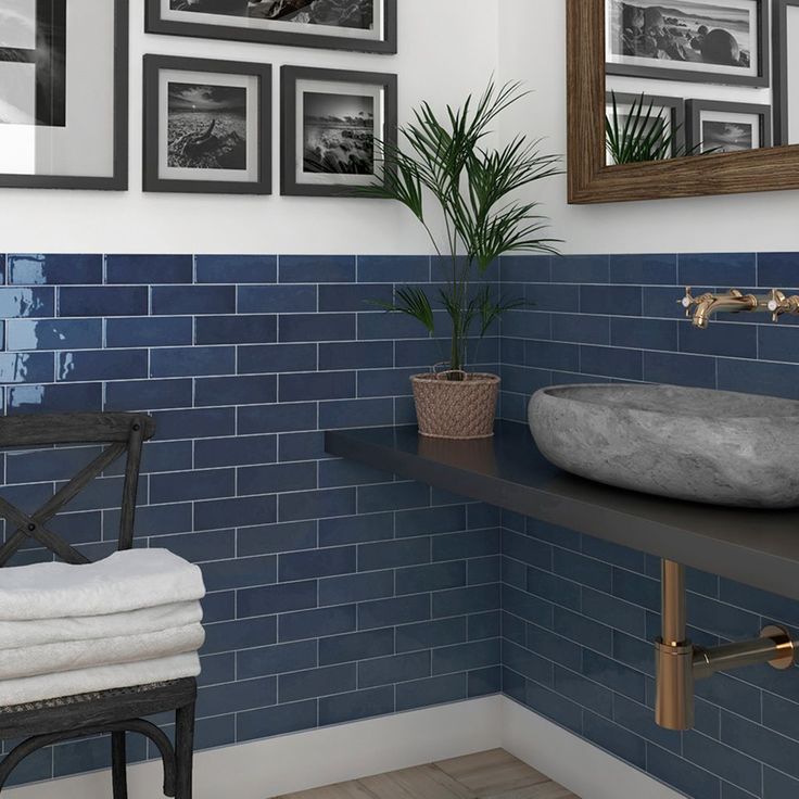 a bathroom with blue tiles and pictures on the wall above the sink, along with a chair