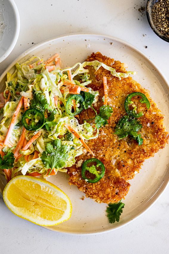 a white plate topped with fried fish next to a lemon wedge and coleslaw