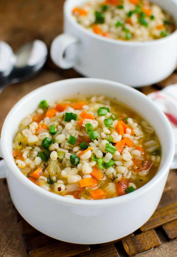 two white bowls filled with rice and vegetables next to spoons on a cutting board