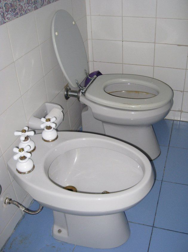 a white toilet sitting next to a bidet in a bathroom on top of a blue tile floor