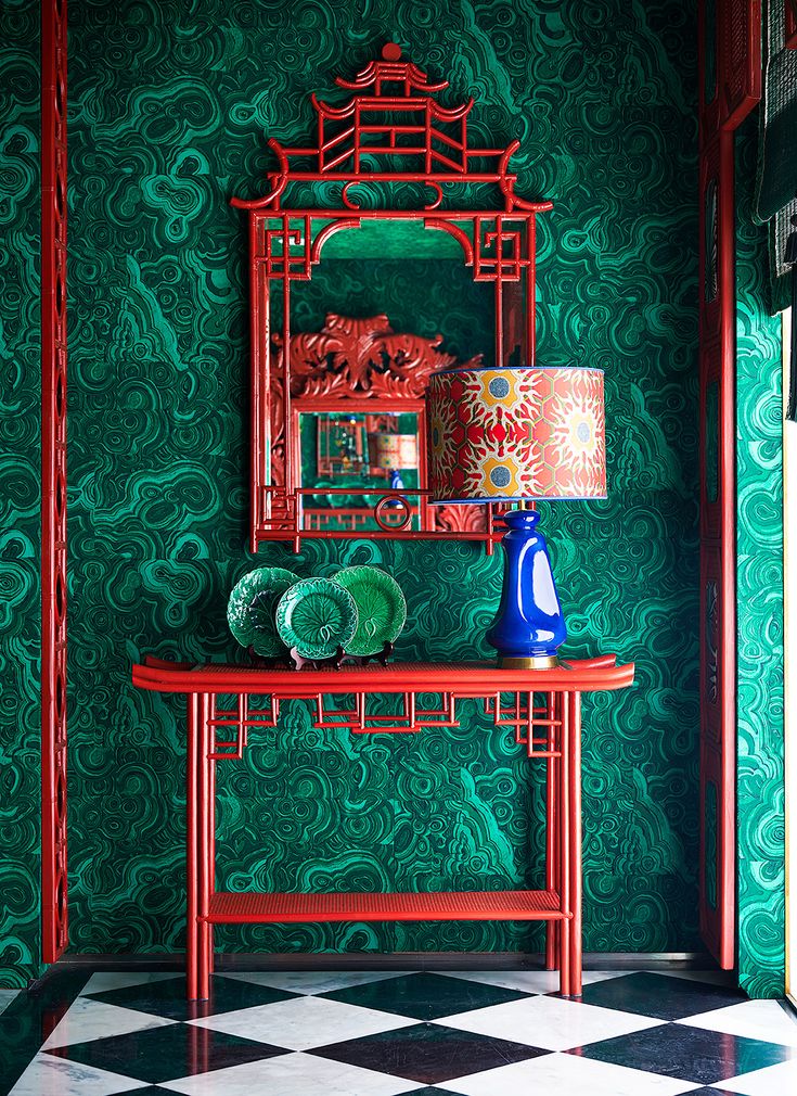 a red table with a blue vase on it in front of a green wall