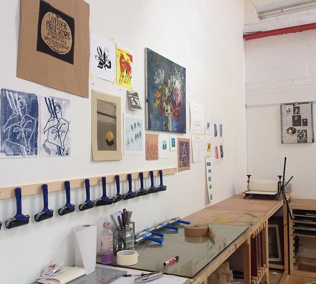 an art studio with various pieces of artwork on the wall and desks lined up against the wall