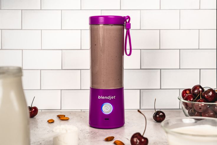 a purple blender sitting on top of a counter next to a bowl of cherries