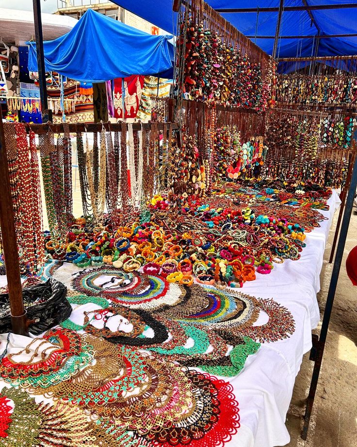 an outdoor market with lots of colorful necklaces and jewelry on display under a blue awning