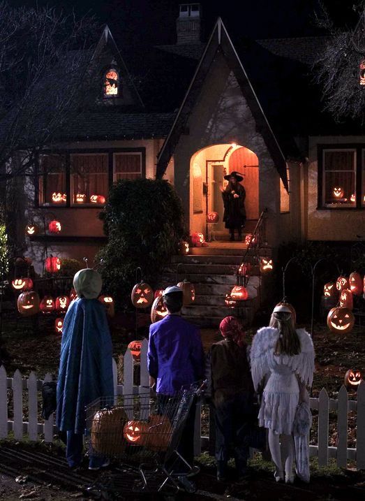 people dressed up in costumes stand outside a house decorated for halloween with pumpkins and jack - o - lanterns