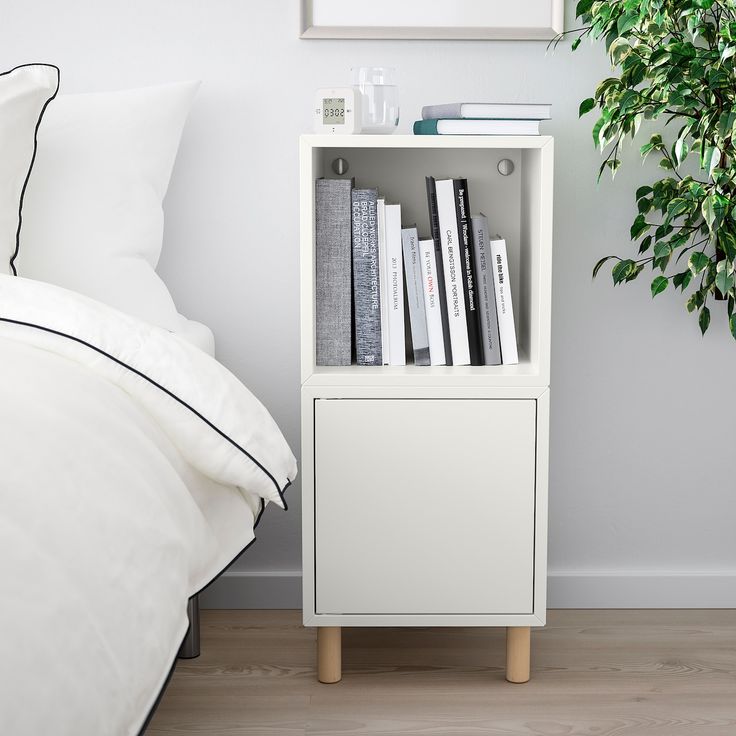 a white book shelf with books on it next to a bed and potted plant