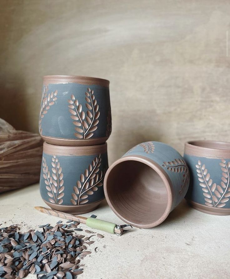 three ceramic cups sitting on top of a table next to some dried leaves and a pencil